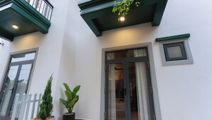 A building with a white exterior, a balcony with green railings, a potted plant, and a sliding glass door. - NiK Hotel Hillside Da Lat (Xuan Huong - Da Lat)