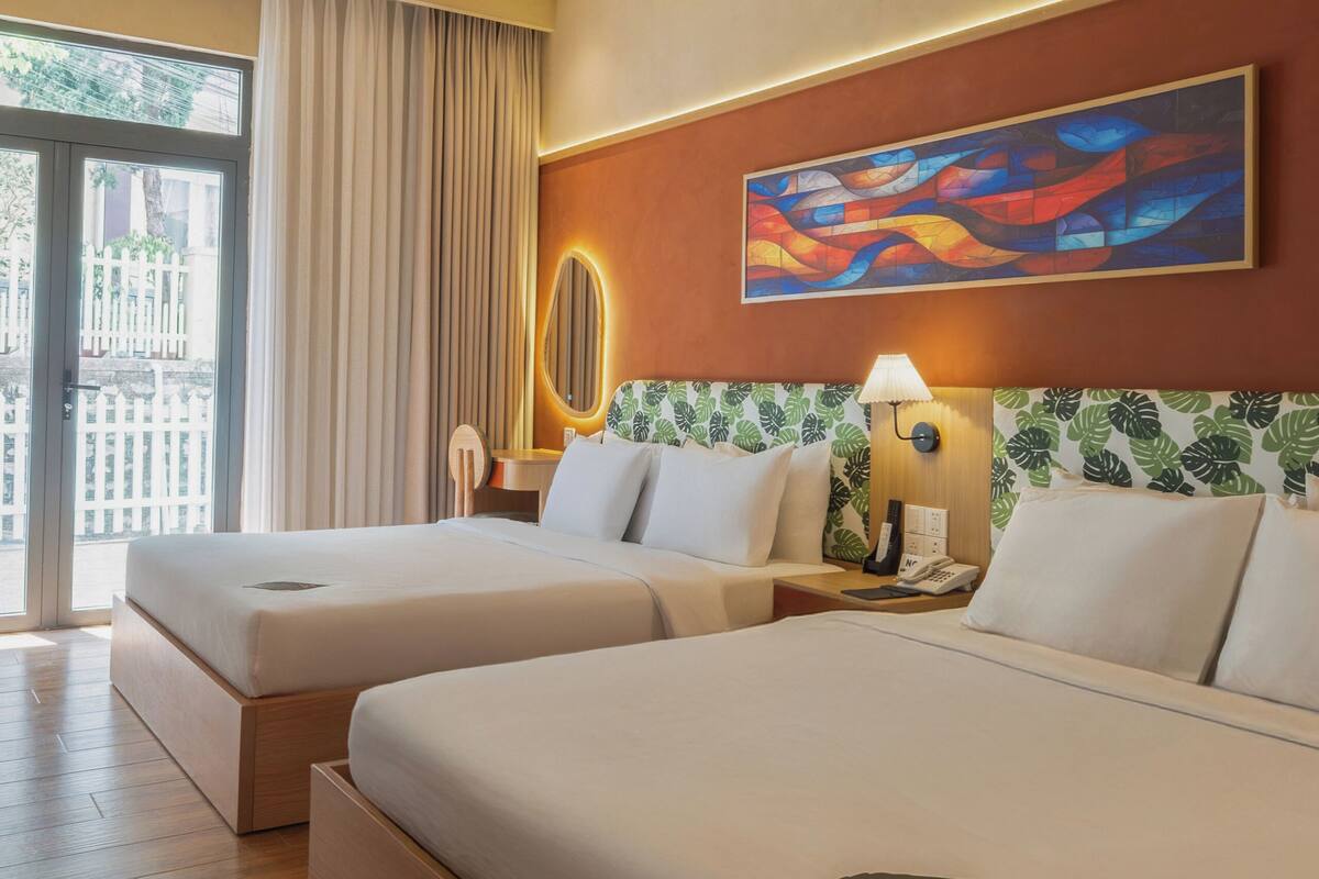 A hotel room with two beds, a large window, a painting on the wall, and a view of the outside.