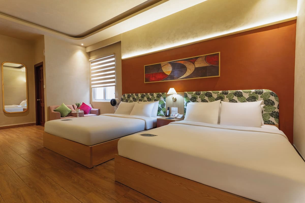 A hotel room with two beds, a mirror, a window with blinds, a wall art piece, and a bedside table with a lamp.