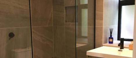 Un baño moderno con ducha de vidrio, tocador de madera y un espejo grande.