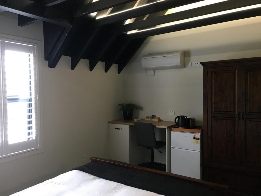 A compact room with a bed, a desk with a chair, a small refrigerator, and a cabinet.