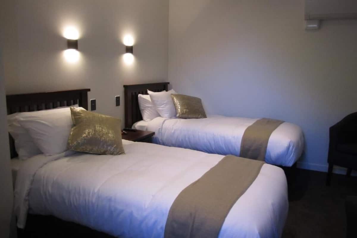 Habitación de hotel con dos camas, cada una con cabecero, mesitas de noche e iluminación en la pared.