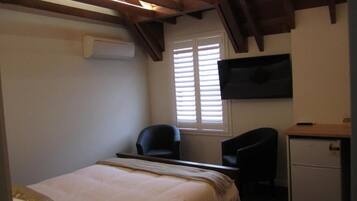 Un dormitorio con cama, dos sillas, un escritorio, televisor y ventana con persianas.