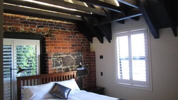 A bedroom with a brick wall, a wooden bed, a window with blinds, and a ceiling with exposed beams.