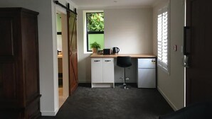Cocina compacta con puerta corredera, un refrigerador pequeño, cafetera y ventana con vista a vegetación.
