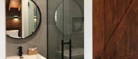 A modern bathroom with a glass shower enclosure, a wooden vanity, and a large mirror.