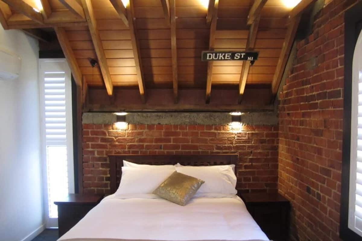 Una habitación con una cama, una pared de ladrillo y un letrero que dice 'DUKE ST N'.