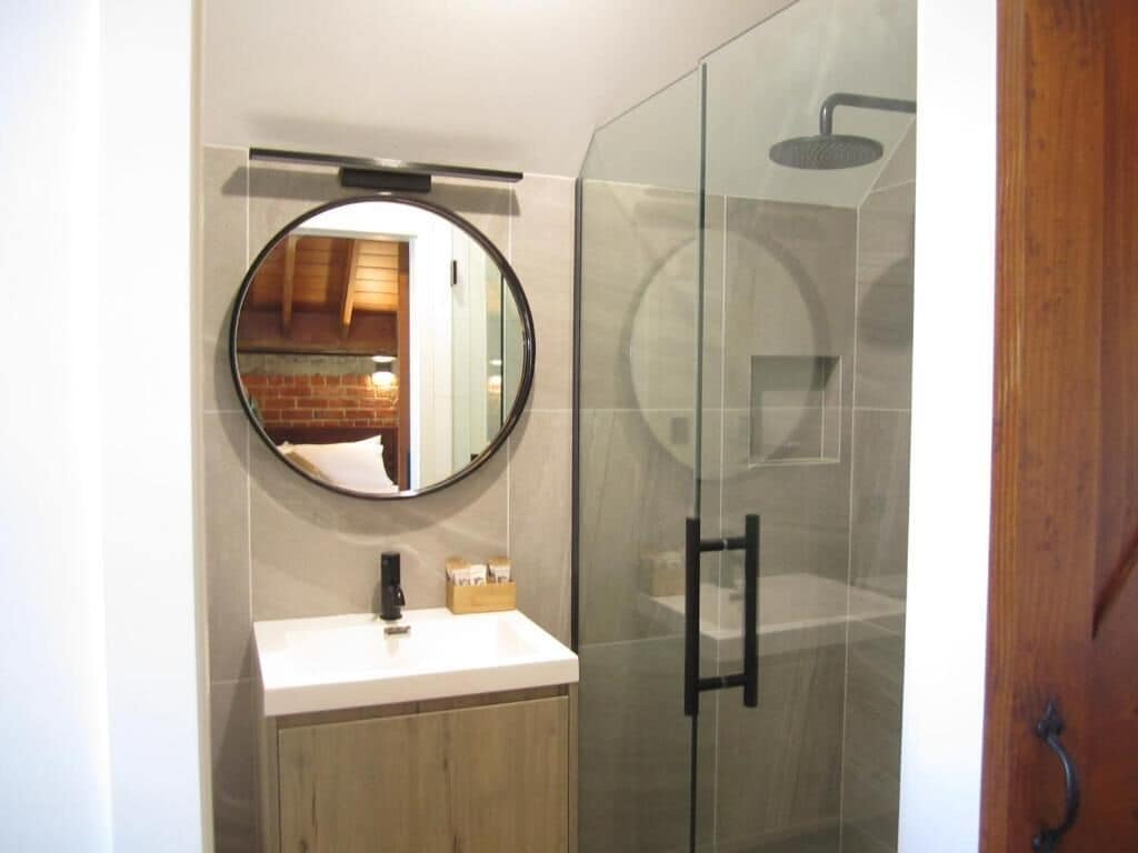A bathroom with a round mirror, a sink, and a glass-enclosed shower.