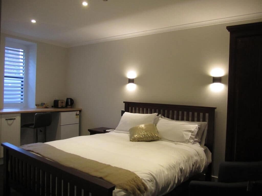 A bedroom with a bed, bedside tables, a desk, and a window with blinds.