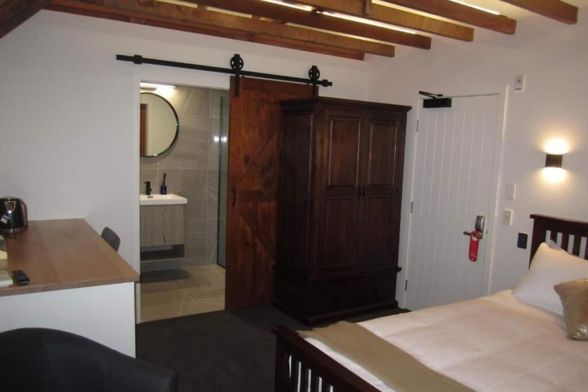 Un dormitorio con cama, armario de madera, escritorio y baño con espejo y lavabo.