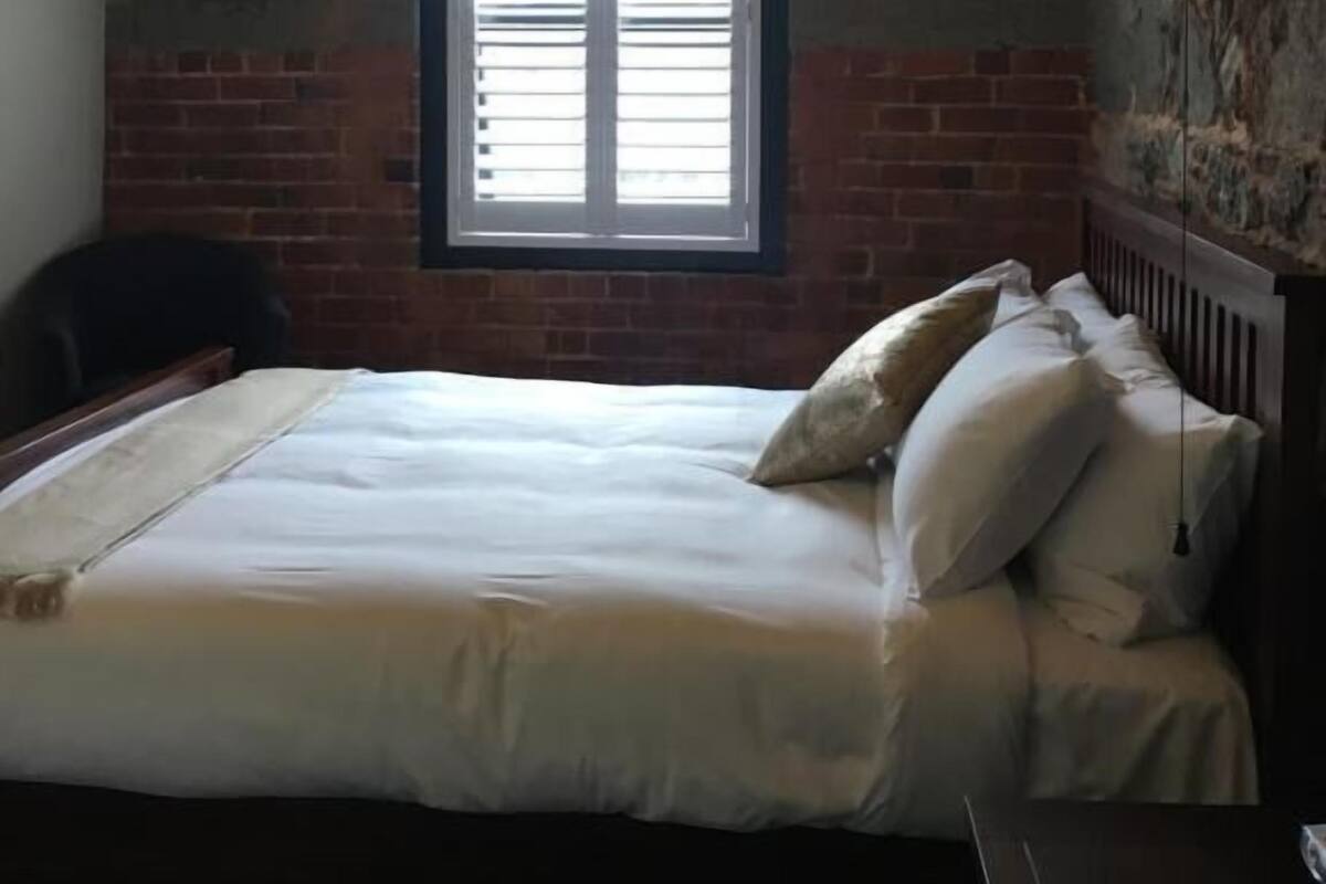 Un dormitorio con una cama, almohadas, una ventana y un cartel sobre la ventana que dice 'QUEEN STN'.