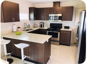 Une cuisine moderne avec des meubles en bois foncé, un îlot central doté de tabourets, un réfrigérateur en acier inoxydable et un four encastré.