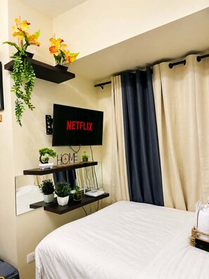 A bedroom with a bed, a TV mounted on the wall, a shelf with plants, and a sign that says 'NETFLIX'.