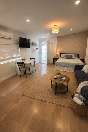 Ein modernes, helles Schlafzimmer mit Bett, Nachttisch und einem an der Wand befestigten Fernseher.