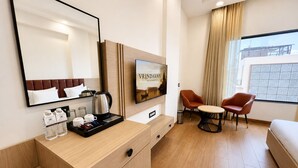 A hotel room with a bed, a TV, a desk with a tray of amenities, a chair, and a window with a view. - Shri ji vilas (Vrindavan)