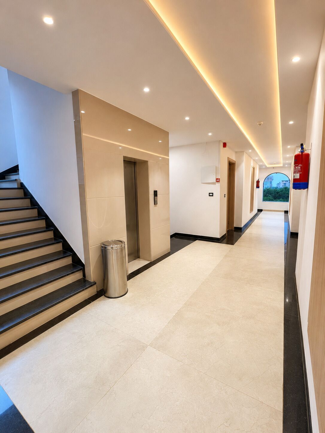 A hotel corridor with a staircase, an elevator, a trash bin, and a fire extinguisher.