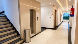 A hotel corridor with a staircase, an elevator, a trash bin, and a fire extinguisher. - Shri ji vilas (Vrindavan)