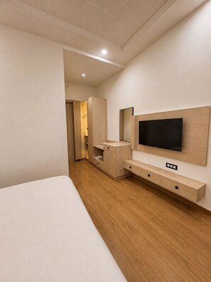 A modern hotel room with a large bed, a TV mounted on the wall, and a wooden wardrobe. - Shri ji vilas (Vrindavan)