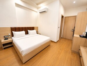 A hotel room with a bed, a bedside table, a wardrobe, and an air conditioning unit. - Shri ji vilas (Vrindavan)