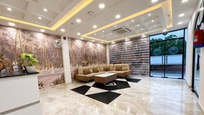 A modern lobby with a beige sofa, a coffee table, and a patterned wall. - Shri ji vilas (Vrindavan)