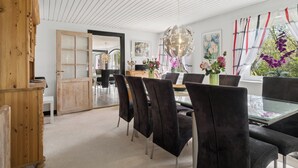 Un coin repas avec une table en verre, des chaises noires, un meuble en bois et une vue sur l’extérieur par une fenêtre agrémentée de rideaux.
