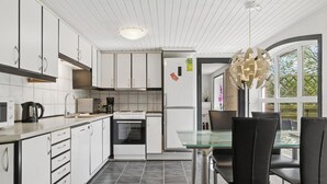 Une cuisine moderne avec des meubles blancs, une table à manger en verre et un luminaire suspendu original.
