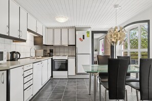 A modern kitchen with white cabinets, a glass dining table, and a unique pendant light. - Spacious holiday home near Limfjord and nature (Øster Assels)