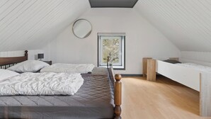 Une chambre avec un plafond en pente, une fenêtre et deux lits.