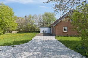 Une allée de gravier mène à un bâtiment en briques, avec un petit abri de jardin en arrière-plan.