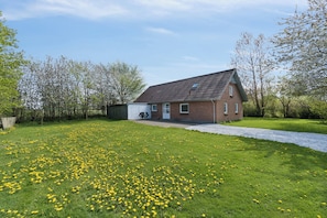 A brick house with a sloped roof, a paved driveway, and a grassy area with yellow flowers.