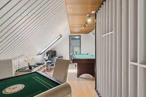 A pool table in a room with a sloped ceiling and a view of a billiards table in the background.