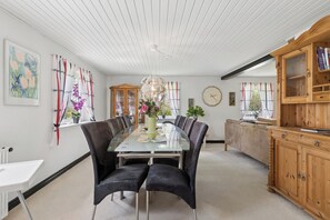 A dining area with a glass table, black upholstered chairs, a wooden cabinet, and a clock on the wall.
