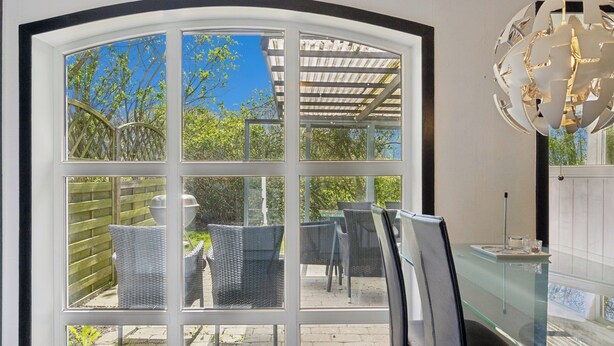 Une véranda avec une table et des chaises en verre, un plafond blanc et une vue sur l’extérieur.