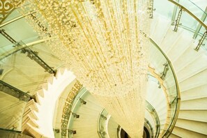 A spiral staircase with a glass railing and a chandelier. - Tianbao Hotel (Fushun)