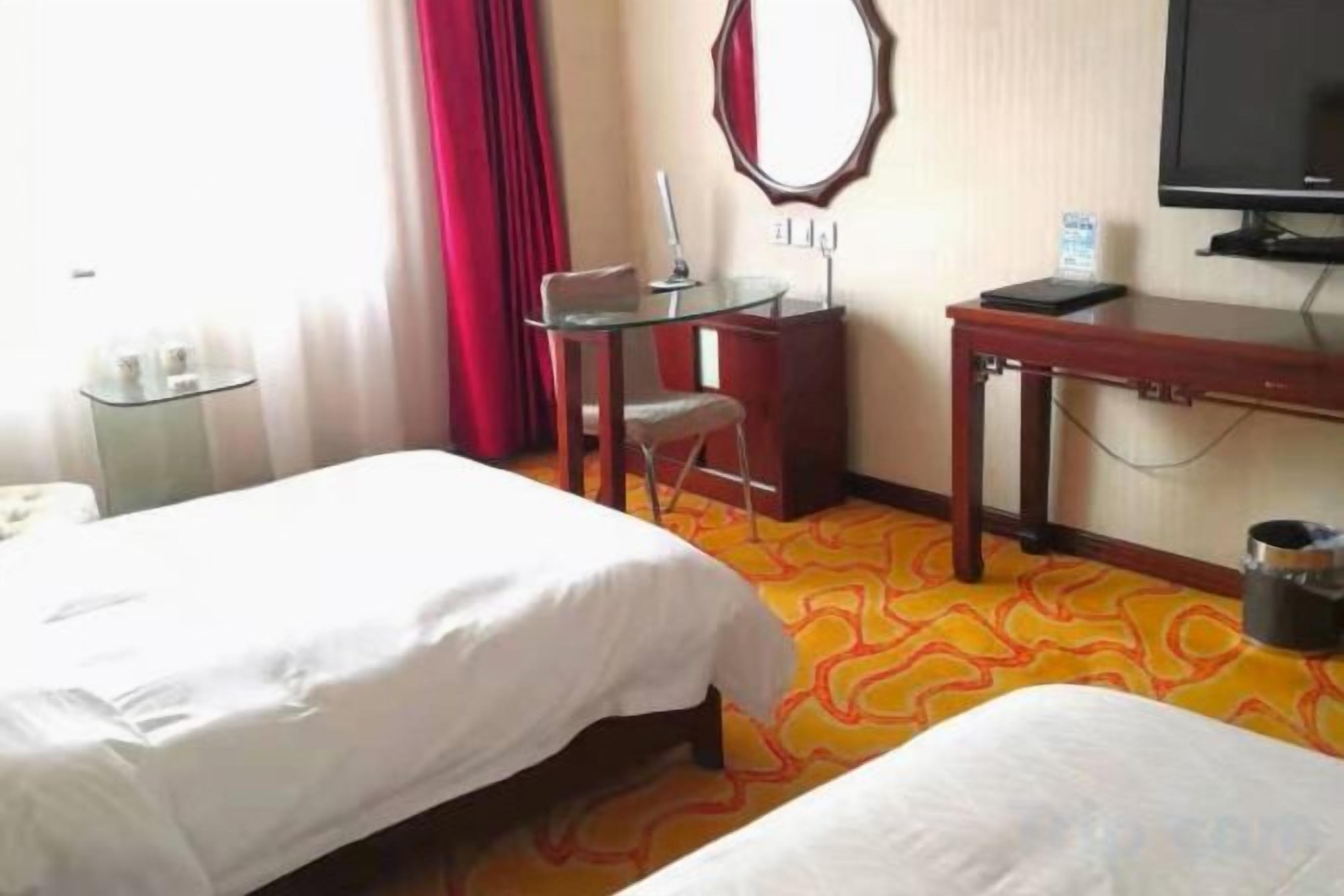 Una habitación de hotel con dos camas, un escritorio, una silla, un televisor y una cortina roja.