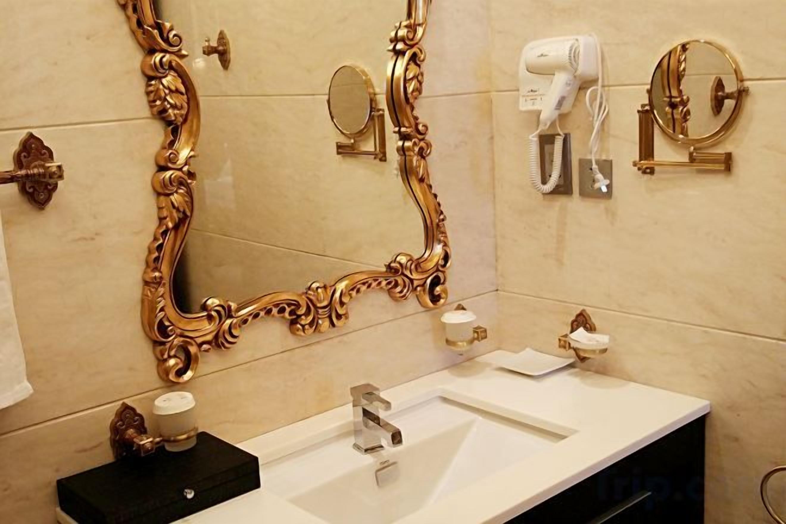 A bathroom with a large ornate mirror, a white sink, and a hairdryer mounted on the wall.