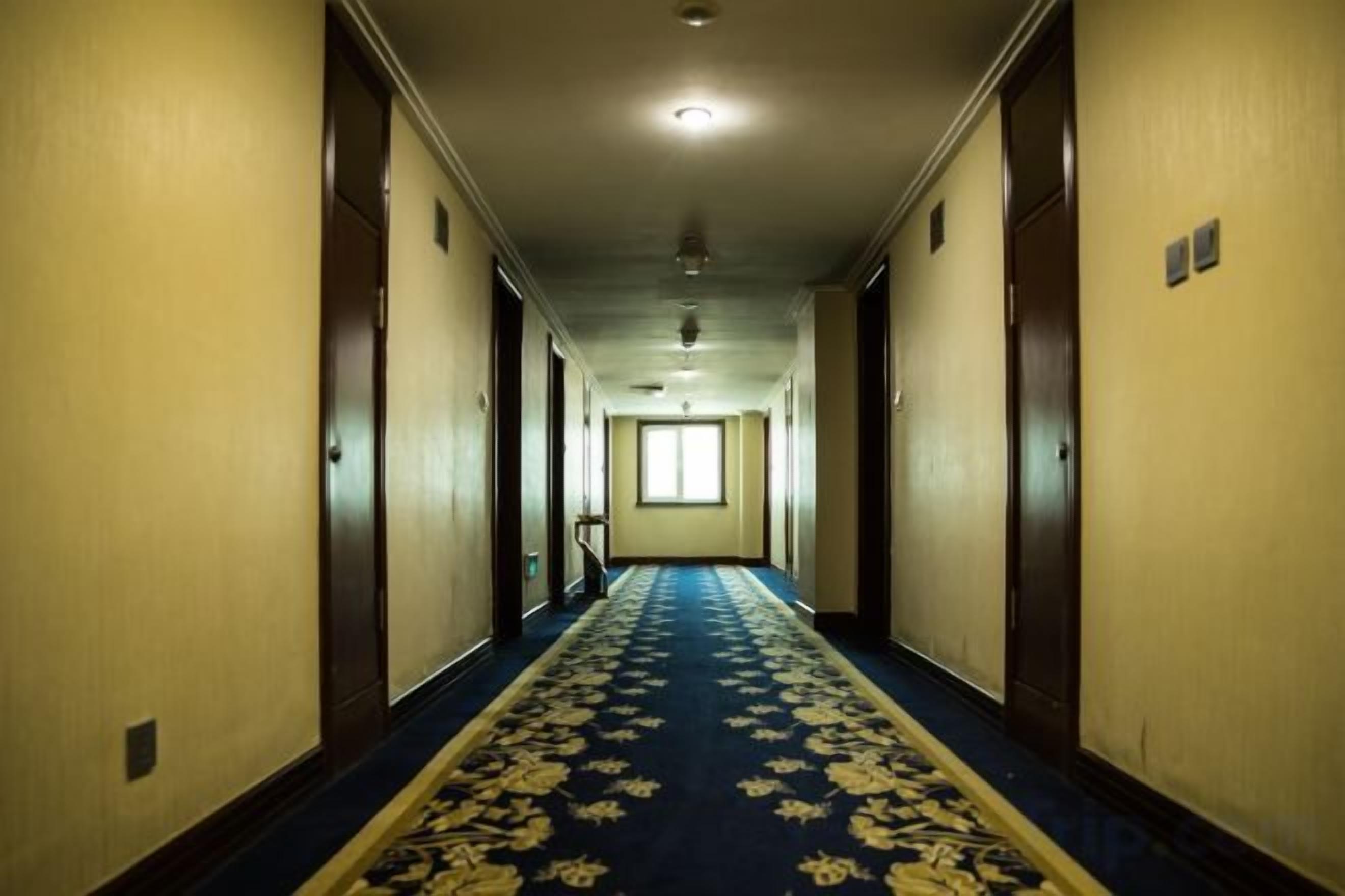 Un pasillo de hotel con piso alfombrado, puertas a ambos lados y un ventanal al final.