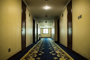 Un pasillo de hotel con piso alfombrado, puertas a ambos lados y un ventanal al final.