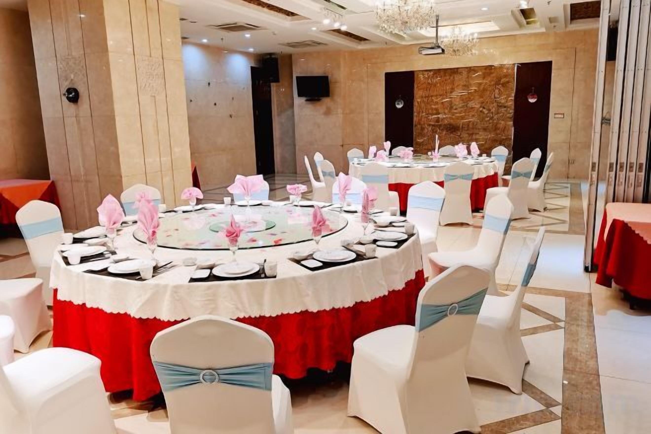 A banquet hall with round tables set for a formal event, white chairs with blue sashes, and a red tablecloth.