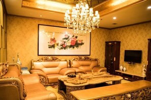 A luxurious room with a large sofa, a coffee table, a chandelier, and a framed artwork on the wall. - Tianbao Hotel (Fushun)