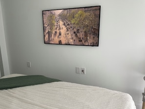 Een slaapkamer met een bed, een aan de muur hangend schilderij en een stopcontact.