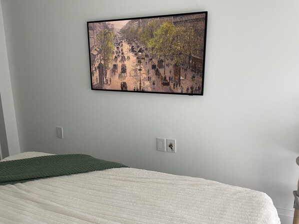 A bedroom with a bed, a wall-mounted painting, and a power outlet. - Madison & East 53rd (New York)