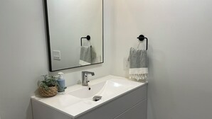 A bathroom with a white sink, a mirror, a towel rack, a plant, and a toilet paper holder.