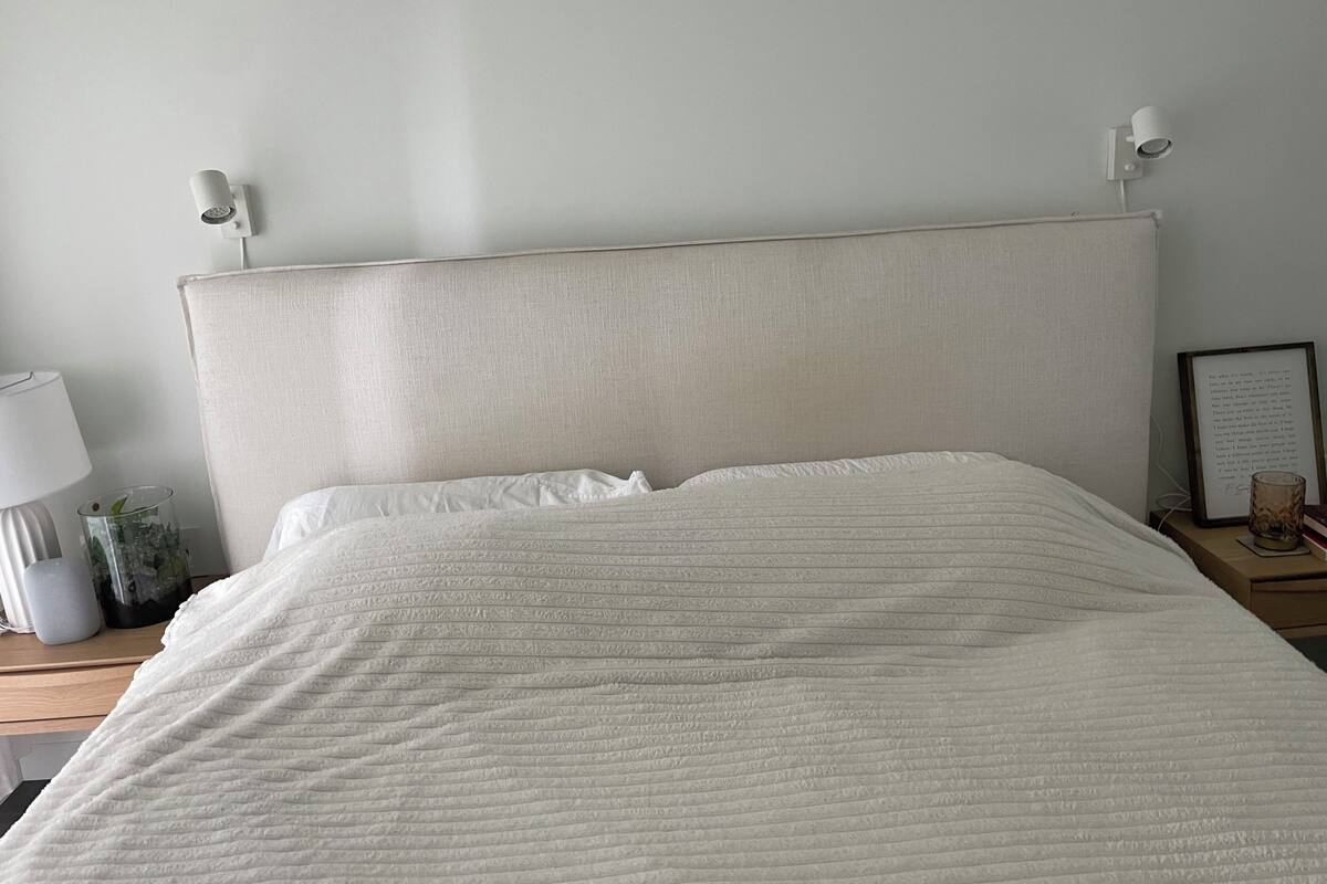 A bed with a textured white headboard, a bedside lamp, a framed picture, and a small vase on a nightstand.