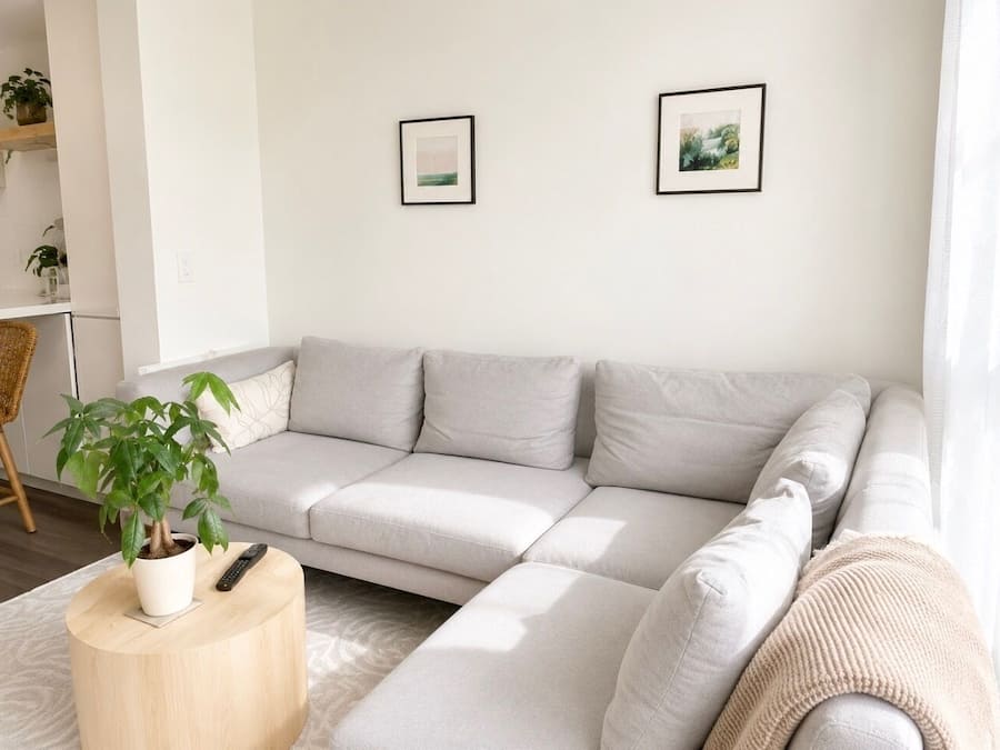 A modern living room with a light-colored sectional sofa, a round wooden coffee table with a potted plant, and two framed pictures on the wall.