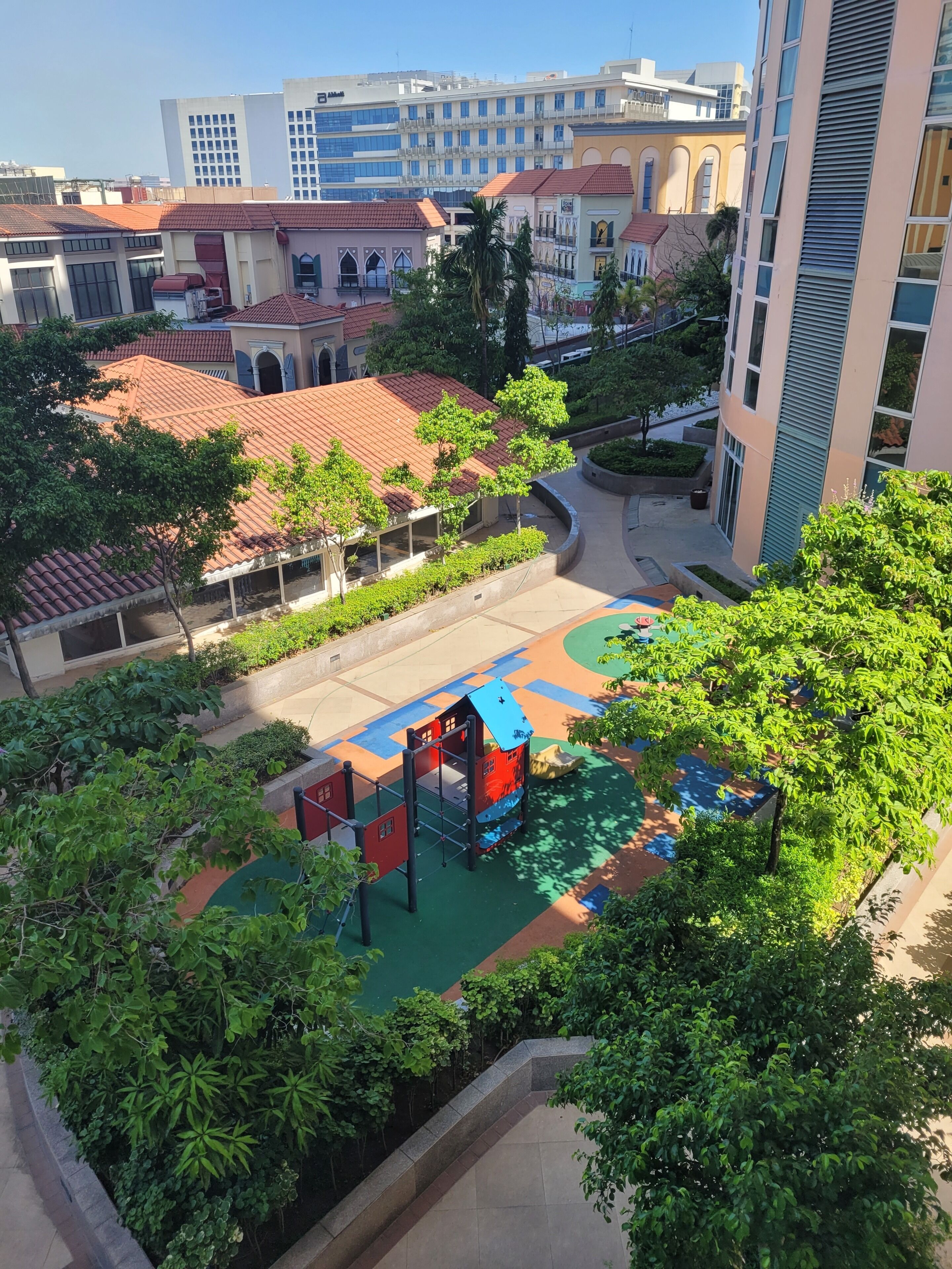 Un cortile con un'area giochi, circondato da edifici con tetti in tegole rosse e vegetazione.