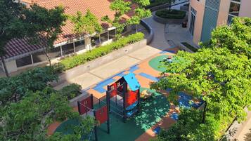 Un cortile con un'area giochi, circondato da edifici con tetti in tegole rosse e vegetazione.
