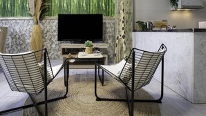 Una sala de estar moderna con un televisor de pantalla plana, dos sillas de estructura metálica, una mesa de centro y una pared decorativa con motivos de bambú y jirafa.