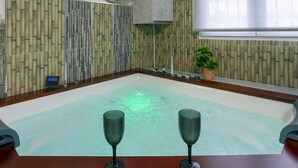 Un cuarto de spa con un jacuzzi grande, dos copas de vino, un panel de control y una pared con diseño de bambú.