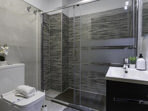 Casa de banho moderna com cabine de duche em vidro, sanita branca e toucador com lavatório e espelho.